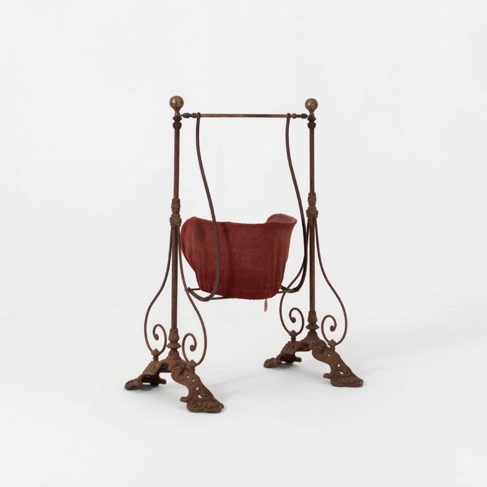 Victorian cast iron freestanding child swing featuring scrolled feet, brass finials, and a red fabric-upholstered suspended seat. View IV