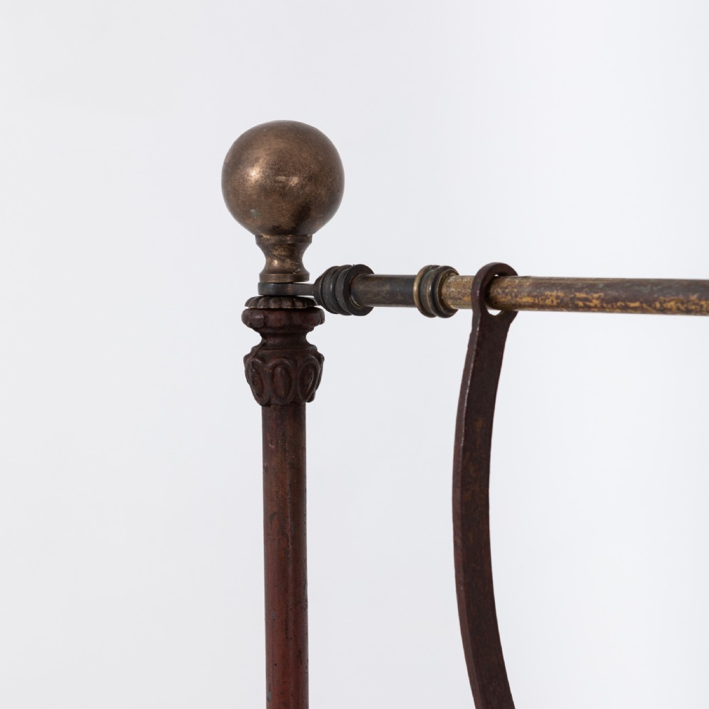 Victorian cast iron freestanding child swing featuring scrolled feet, brass finials, and a red fabric-upholstered suspended seat. View VII