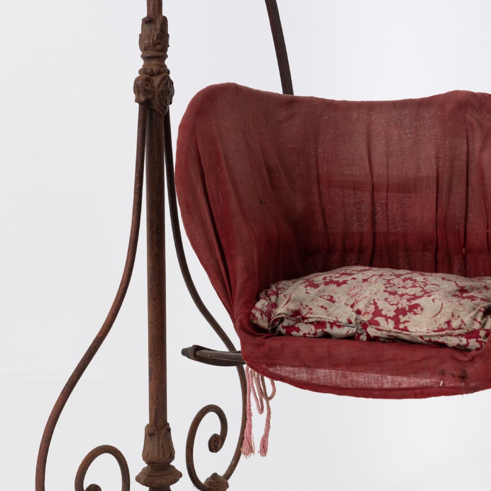 Victorian cast iron freestanding child swing featuring scrolled feet, brass finials, and a red fabric-upholstered suspended seat. View IX