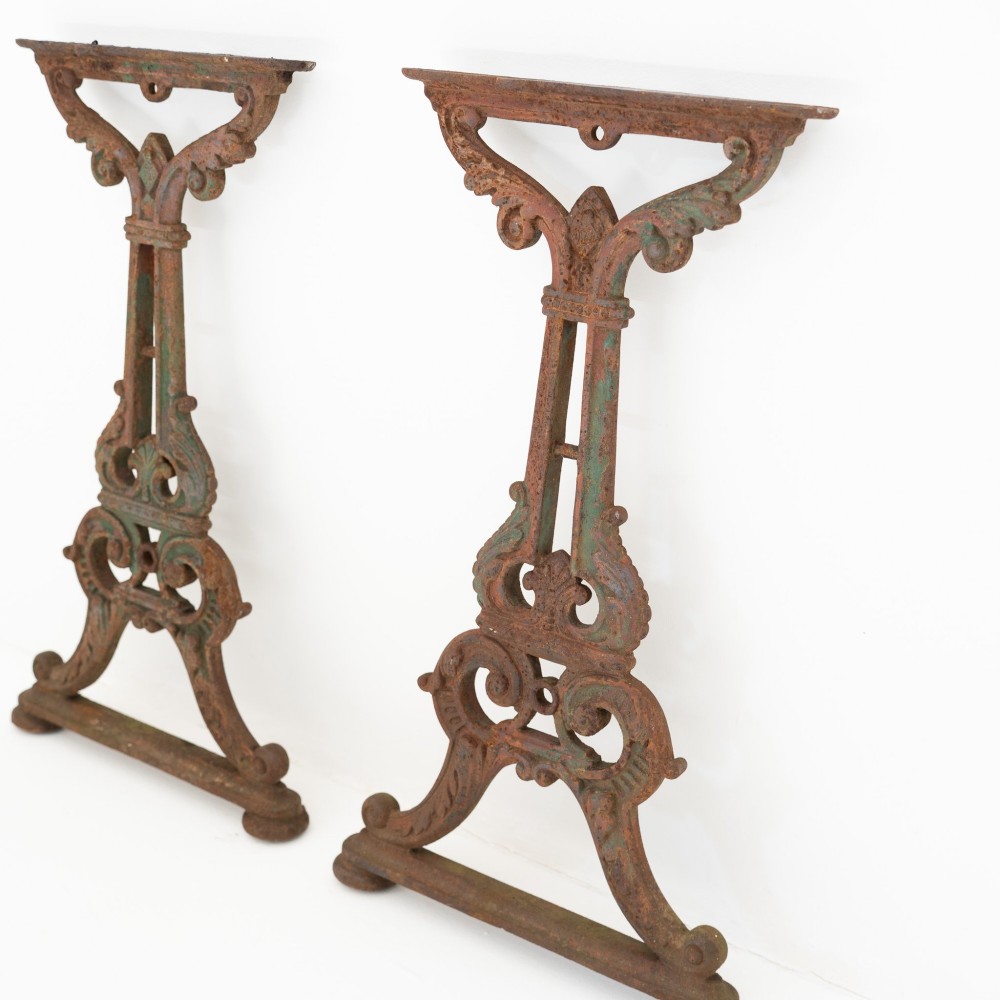 A pair of ornate Victorian cast iron table bases featuring openwork scrollwork and a rusted finish with traces of original green paint. View II