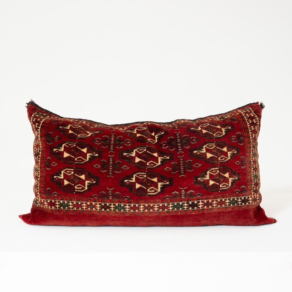 A rectangular hand-woven wool cushion featuring geometric Turkmen gul patterns in deep red, cream, and dark brown.