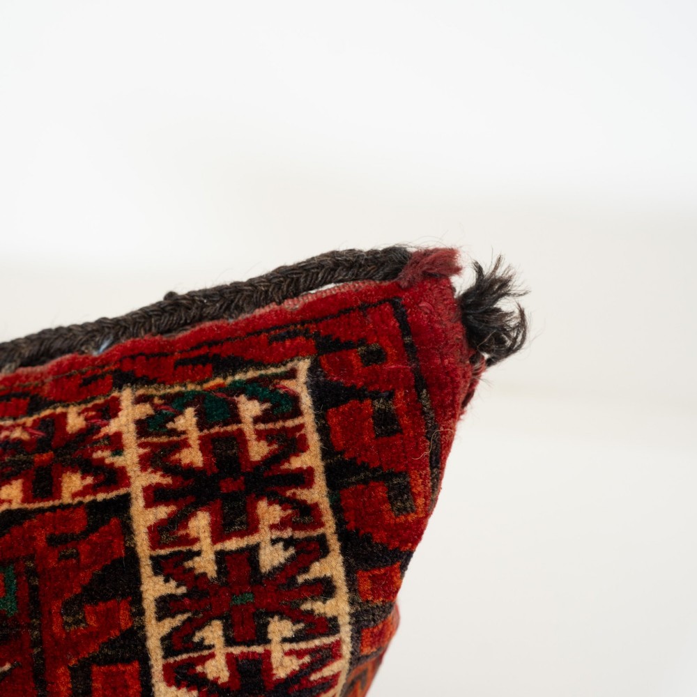 A rectangular hand-woven wool cushion featuring geometric Turkmen gul patterns in deep red, cream, and dark brown. View V
