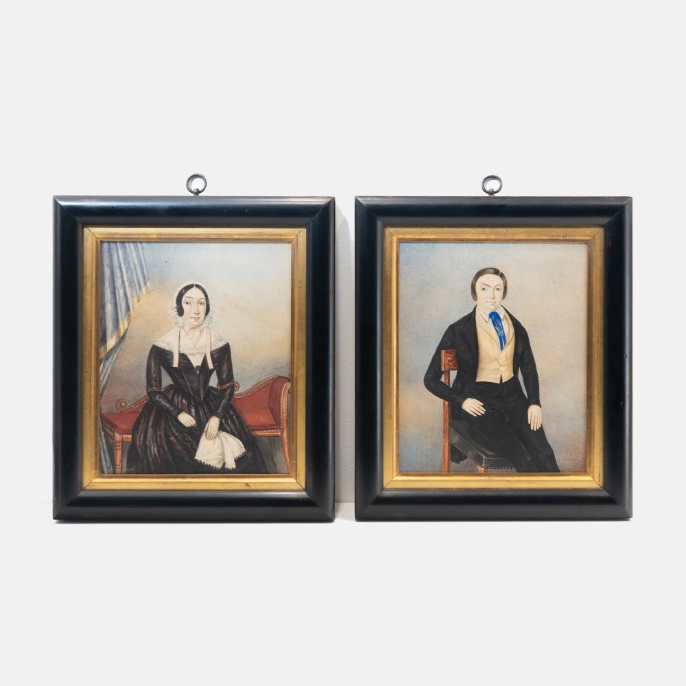 A pair of mid-19th century framed folk art portraits depicting a seated woman and man in period clothing.
