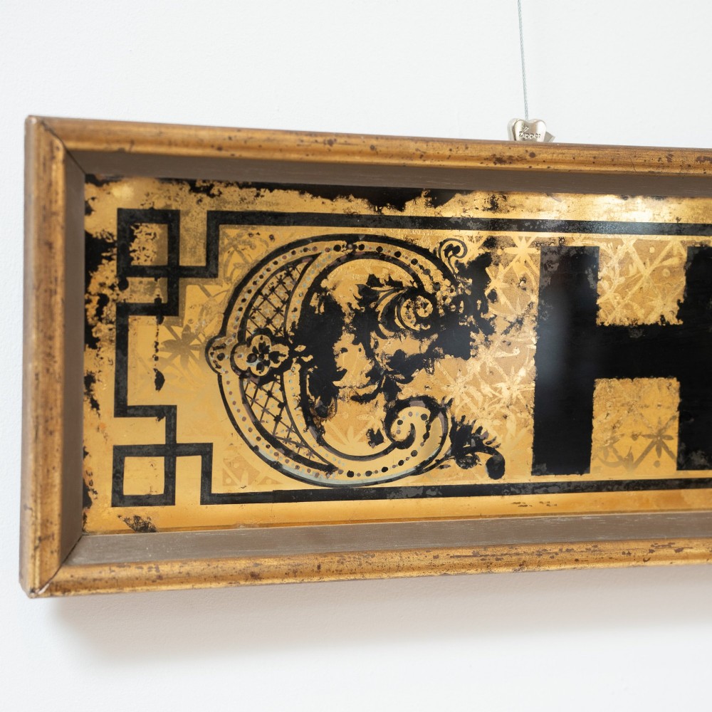 A long rectangular late Victorian verre eglomise glass shop sign framed in gold timber, displaying bold black lettering reading CHEMIST & on a gilded background. View III