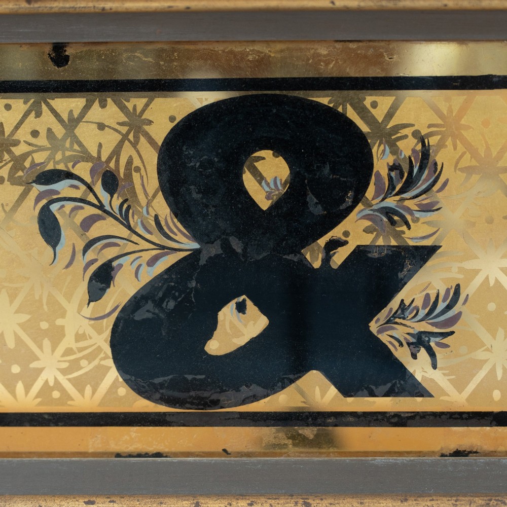 A long rectangular late Victorian verre eglomise glass shop sign framed in gold timber, displaying bold black lettering reading CHEMIST & on a gilded background. View V