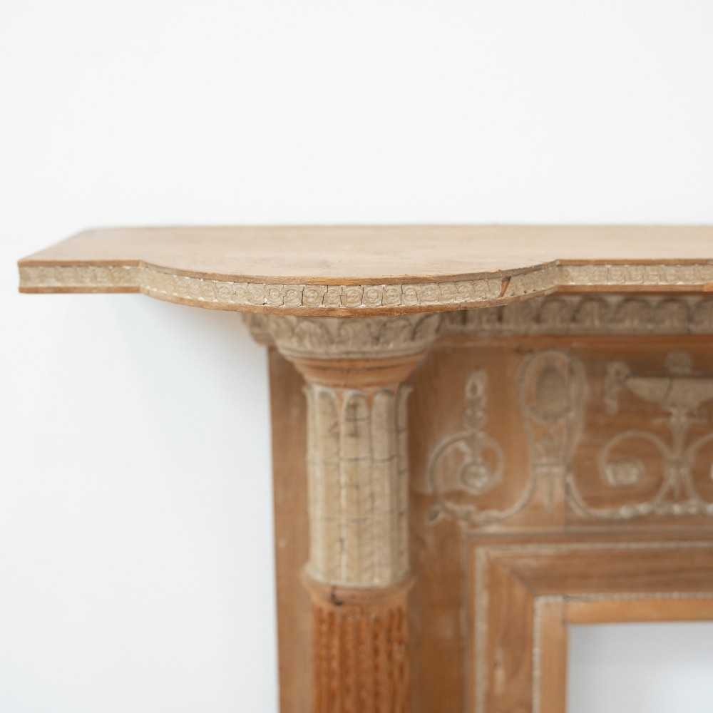A Victorian stripped pine fireplace surround featuring fluted side columns, a stepped mantel shelf, and a central carved panel depicting a chariot scene. View IV