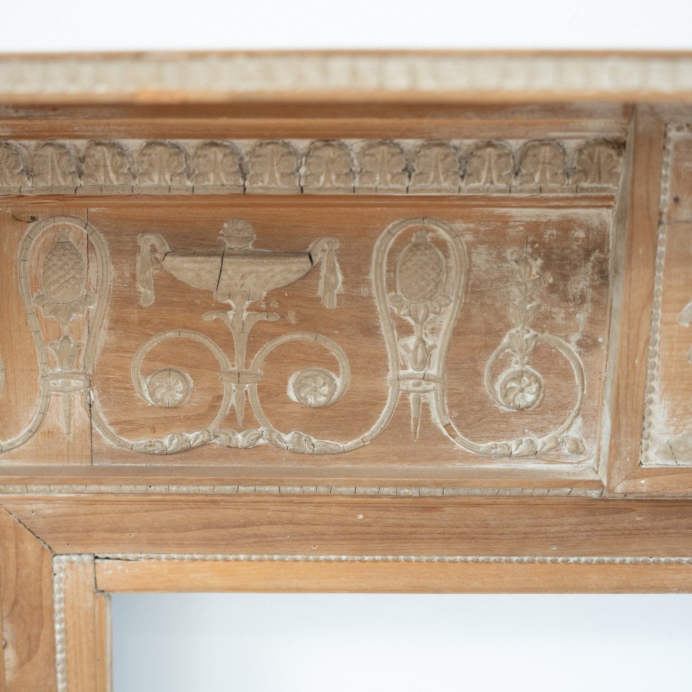 A Victorian stripped pine fireplace surround featuring fluted side columns, a stepped mantel shelf, and a central carved panel depicting a chariot scene. View VI