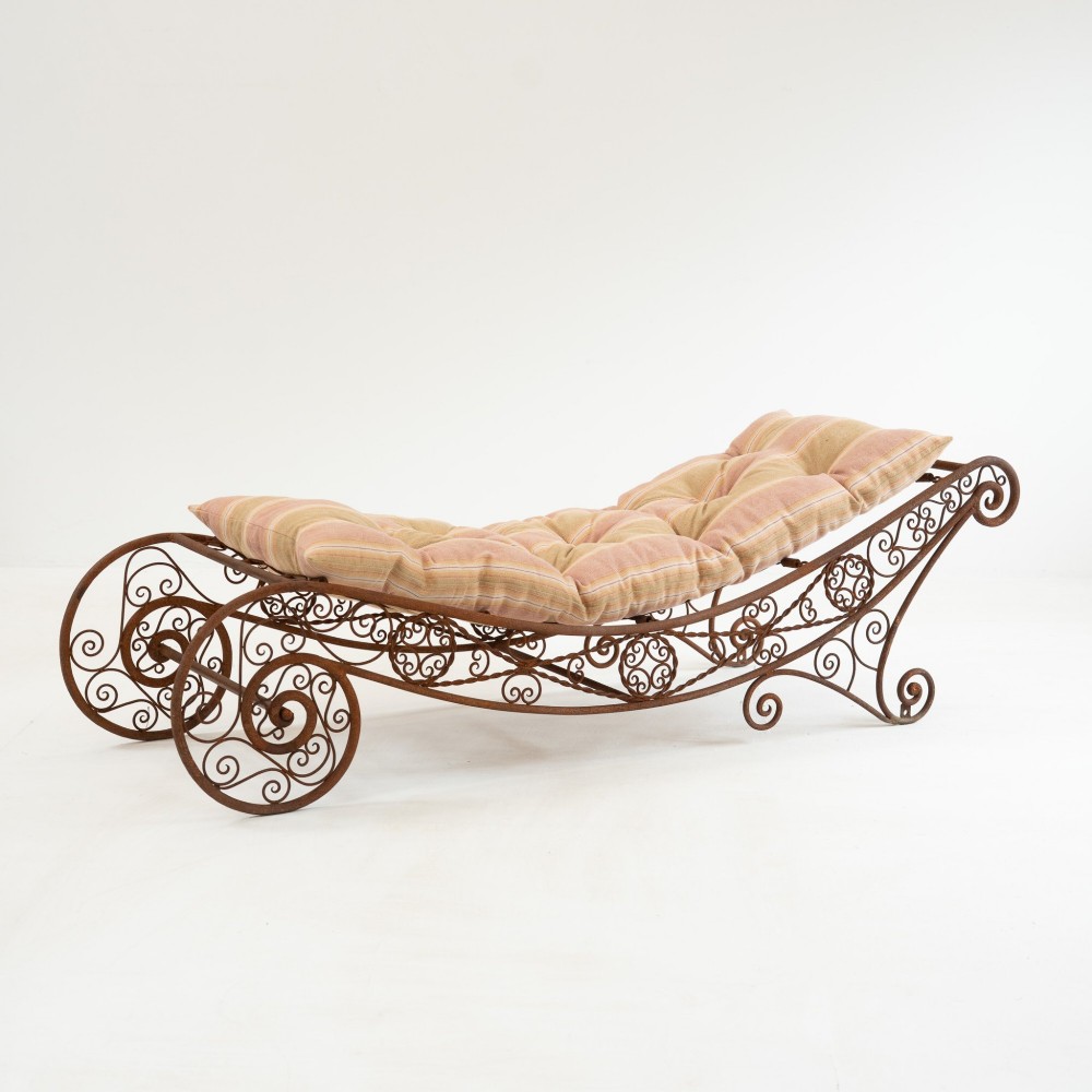 A nineteenth-century French wrought iron garden daybed featuring scrollwork, a contoured reclining frame, and decorative front wheels with a weathered brown patina. View II