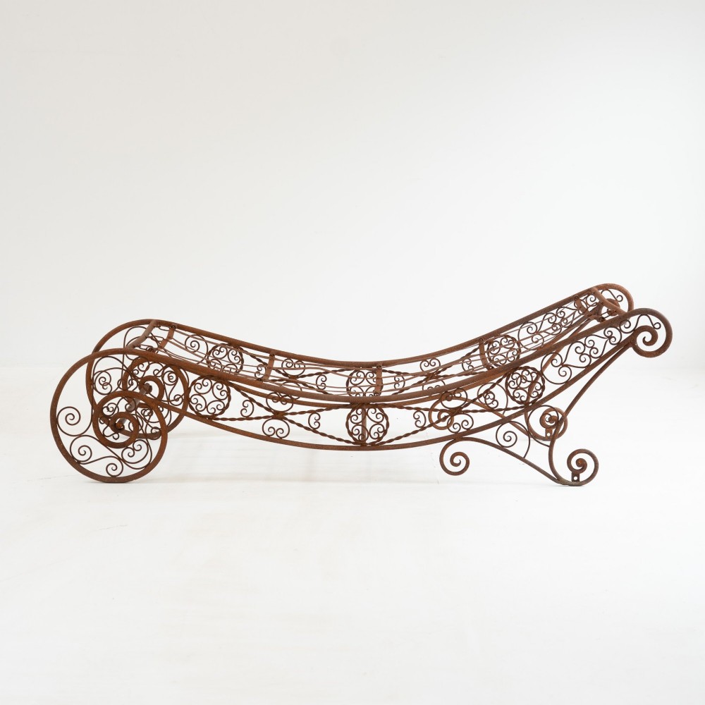 A nineteenth-century French wrought iron garden daybed featuring scrollwork, a contoured reclining frame, and decorative front wheels with a weathered brown patina. View III