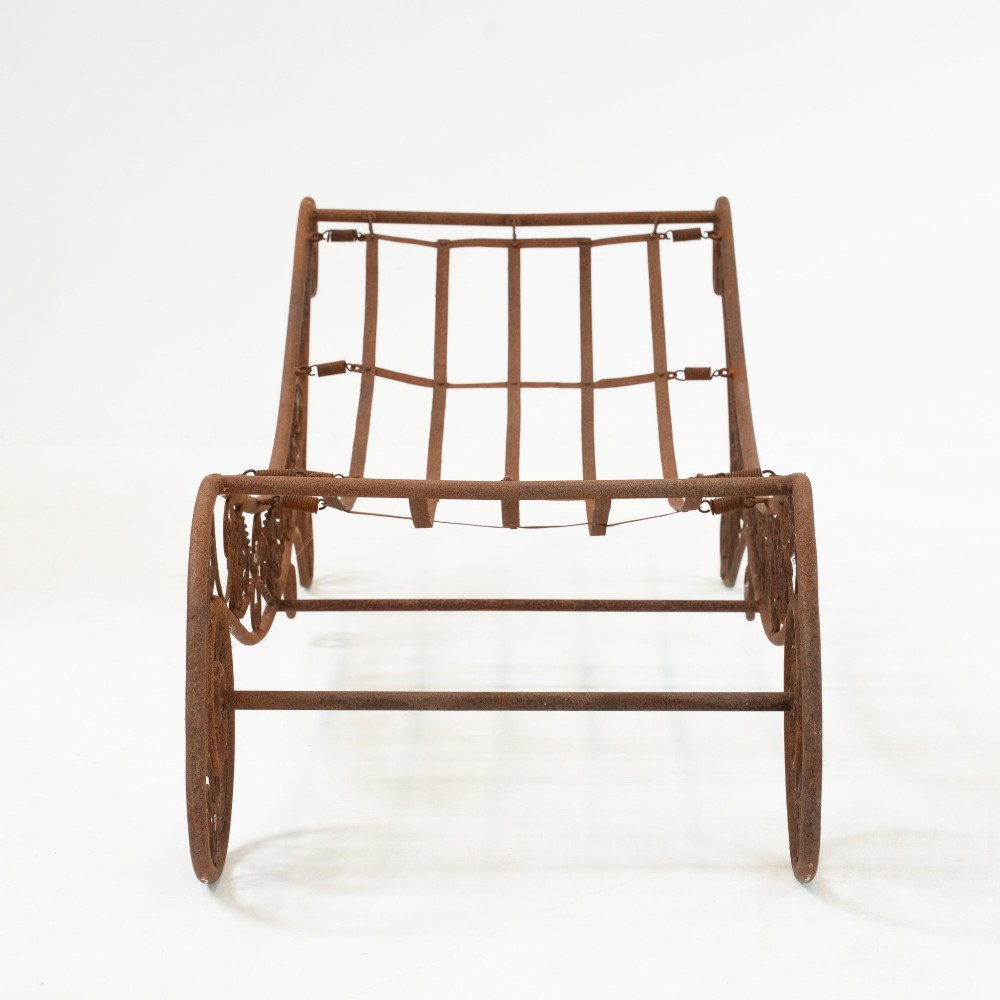 A nineteenth-century French wrought iron garden daybed featuring scrollwork, a contoured reclining frame, and decorative front wheels with a weathered brown patina. View V