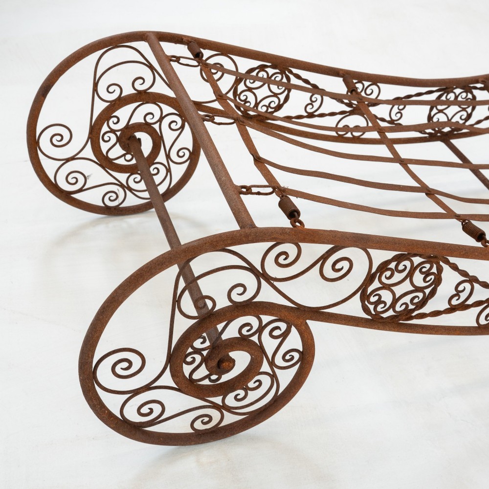 A nineteenth-century French wrought iron garden daybed featuring scrollwork, a contoured reclining frame, and decorative front wheels with a weathered brown patina. View XI