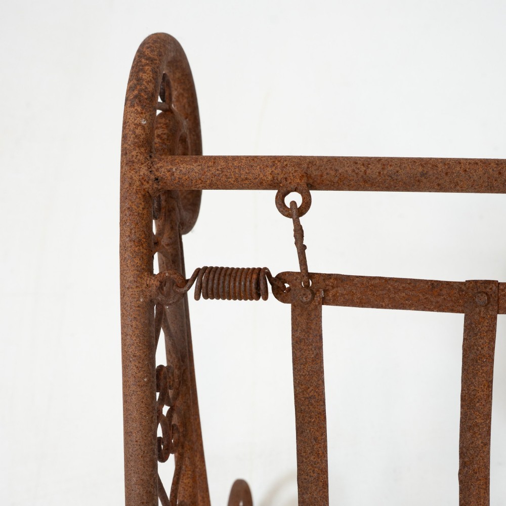 A nineteenth-century French wrought iron garden daybed featuring scrollwork, a contoured reclining frame, and decorative front wheels with a weathered brown patina. View XII