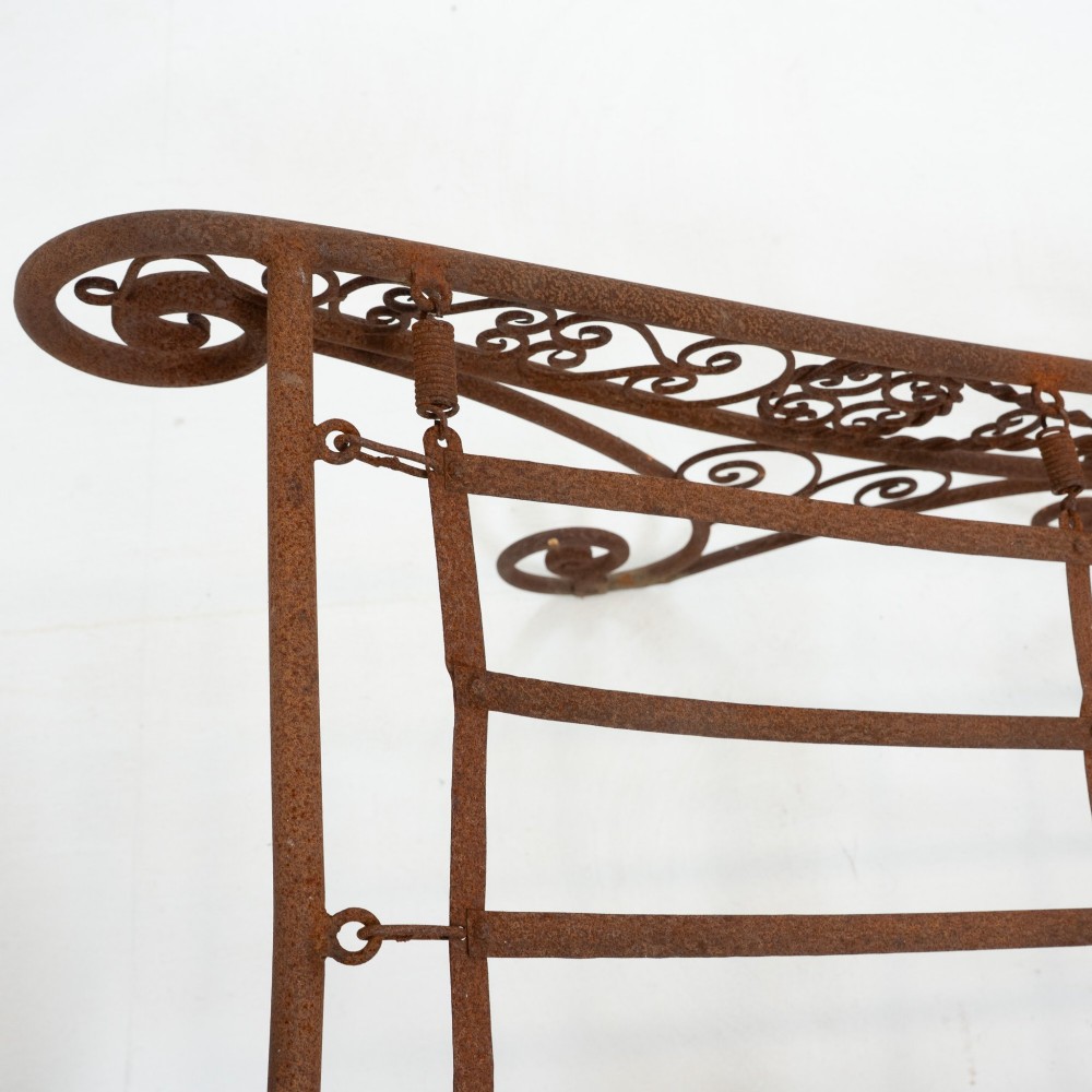 A nineteenth-century French wrought iron garden daybed featuring scrollwork, a contoured reclining frame, and decorative front wheels with a weathered brown patina. View XIII
