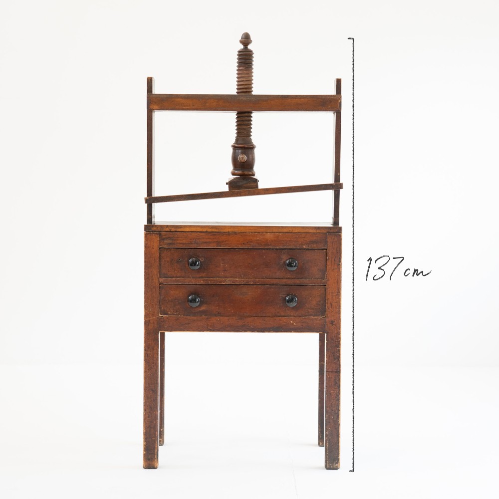 A Victorian mahogany and pine linen press featuring a central wooden screw mechanism over two small drawers with turned black knobs and four square legs. View II