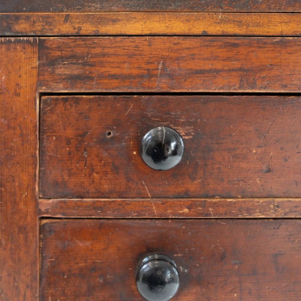 A Victorian mahogany and pine linen press featuring a central wooden screw mechanism over two small drawers with turned black knobs and four square legs. View XV