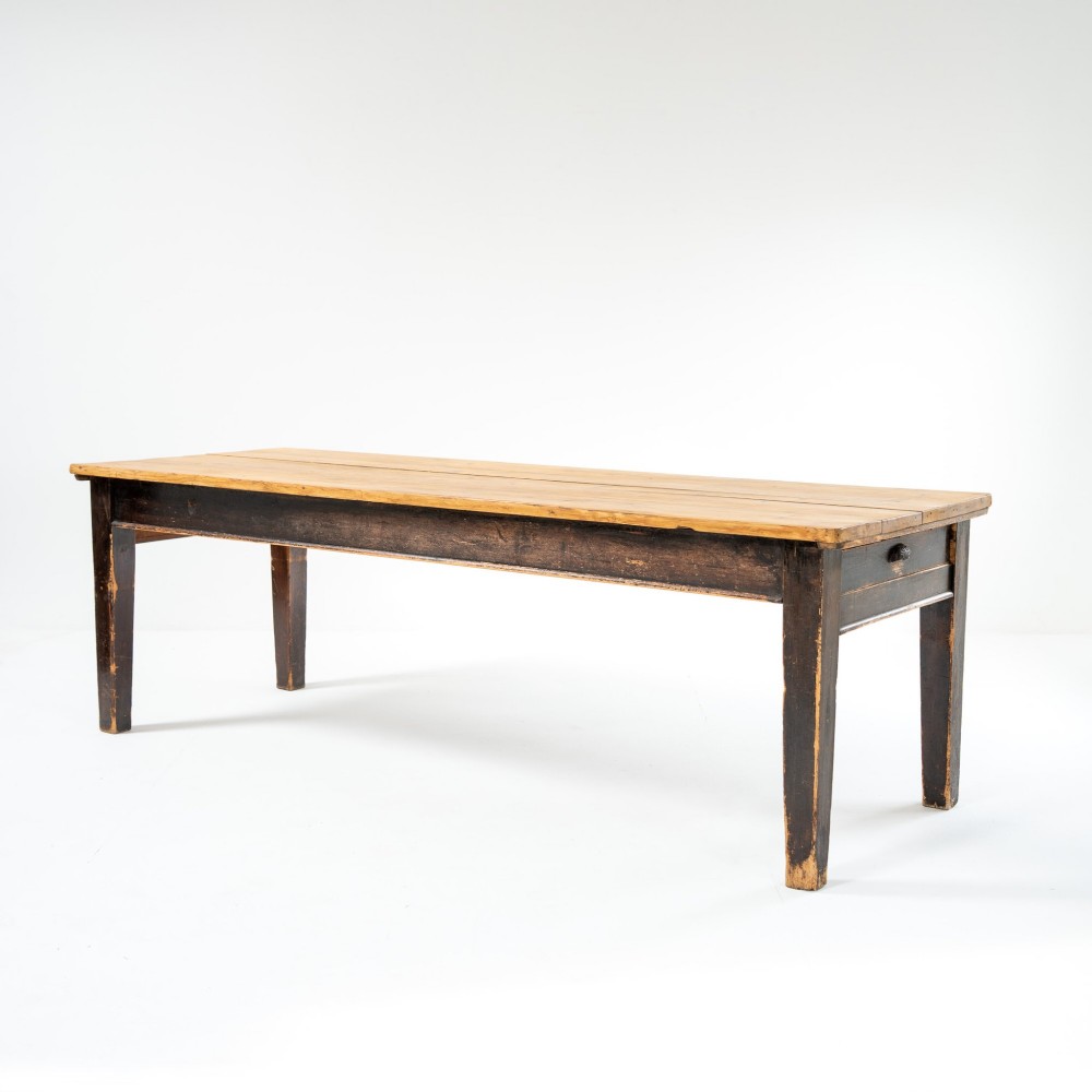 An eight-foot long Victorian pine harvest table featuring a natural timber top surface, a distressed black painted apron, and tapered square legs.