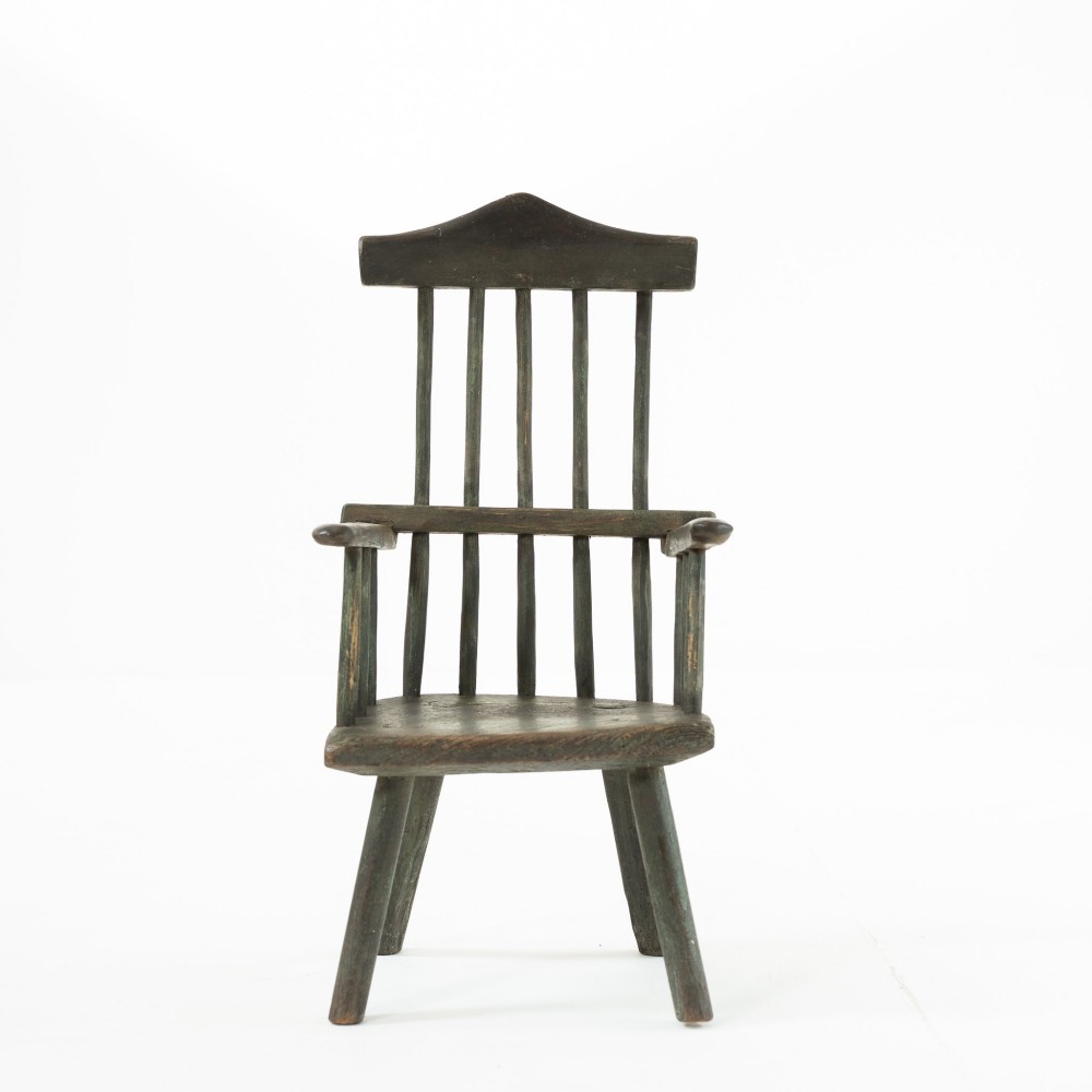 A 19th-century primitive childs stick-back armchair crafted from dark patinated timber with splayed legs and a crest rail. View II