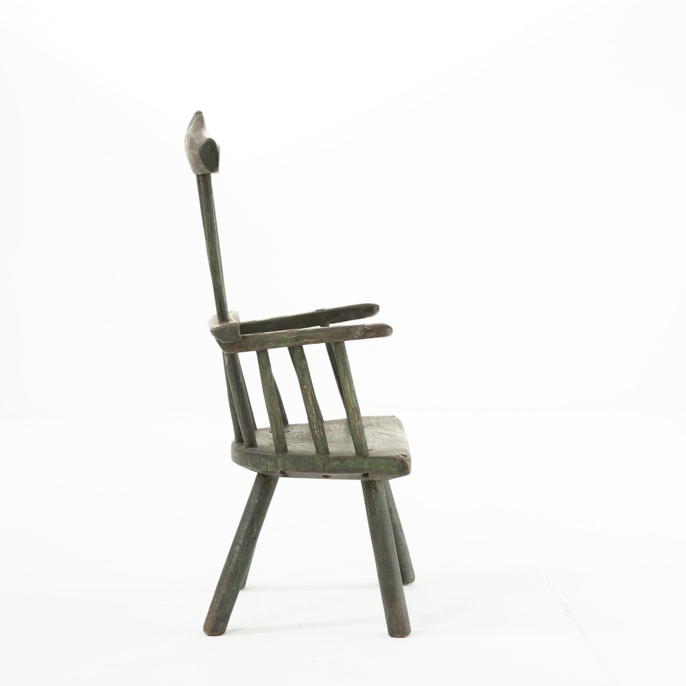 A 19th-century primitive childs stick-back armchair crafted from dark patinated timber with splayed legs and a crest rail. View III