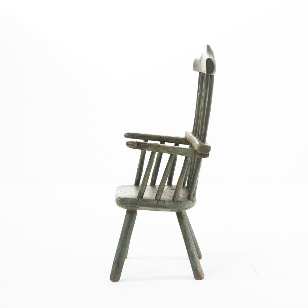 A 19th-century primitive childs stick-back armchair crafted from dark patinated timber with splayed legs and a crest rail. View V
