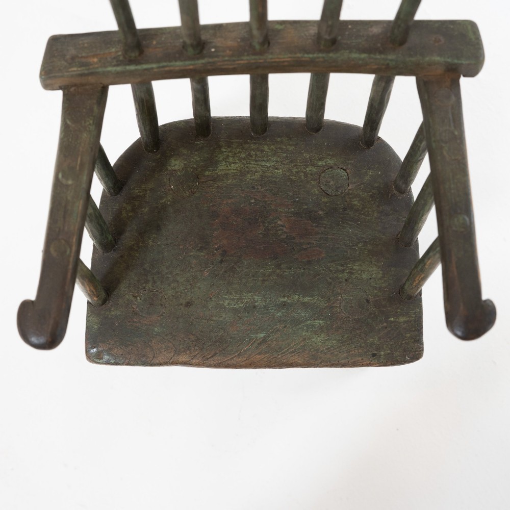 A 19th-century primitive childs stick-back armchair crafted from dark patinated timber with splayed legs and a crest rail. View VII
