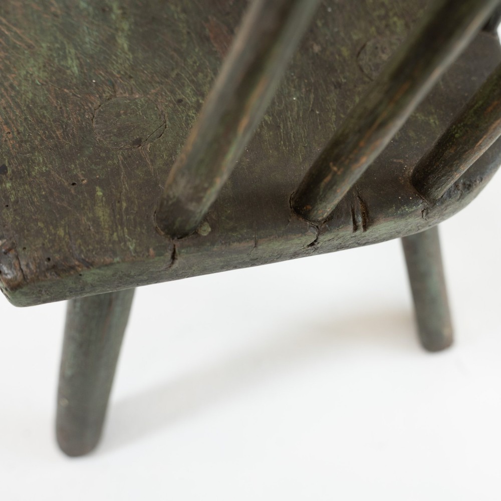 A 19th-century primitive childs stick-back armchair crafted from dark patinated timber with splayed legs and a crest rail. View X