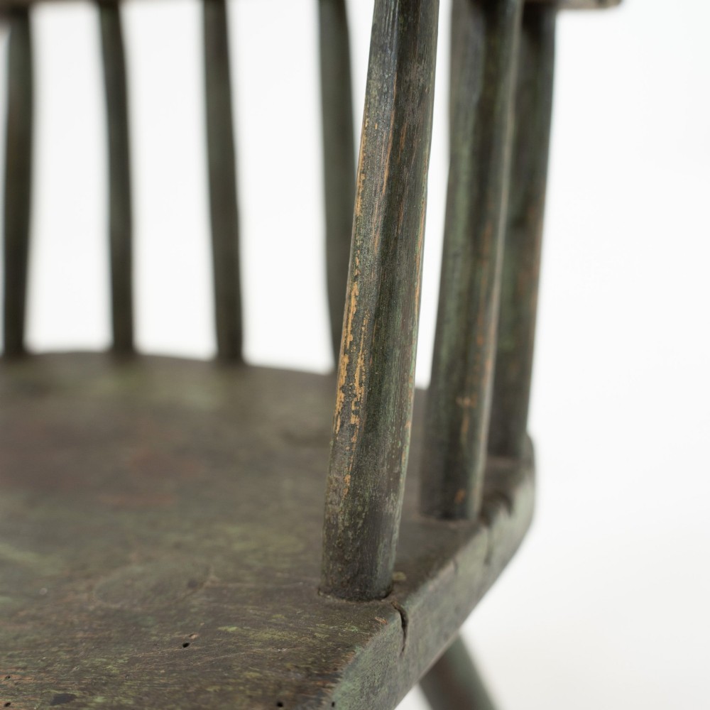 A 19th-century primitive childs stick-back armchair crafted from dark patinated timber with splayed legs and a crest rail. View XV