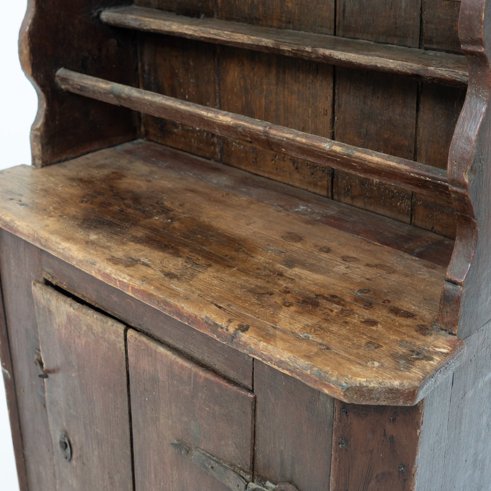 A late eighteenth-century dark timber Irish kitchen dresser featuring open plate shelves with scalloped sides above a single-door cupboard base with wrought iron hinges. View VII