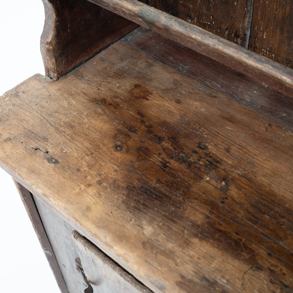 A late eighteenth-century dark timber Irish kitchen dresser featuring open plate shelves with scalloped sides above a single-door cupboard base with wrought iron hinges. View IX