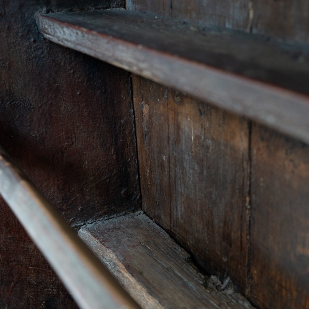 A late eighteenth-century dark timber Irish kitchen dresser featuring open plate shelves with scalloped sides above a single-door cupboard base with wrought iron hinges. View X