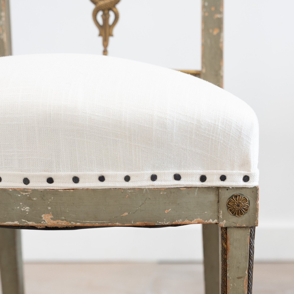 A set of four 19th-century Northern European Neoclassical side chairs featuring distressed grey paintwork, off-white linen upholstery, and gilded caduceus motifs in the open back frames. View XI