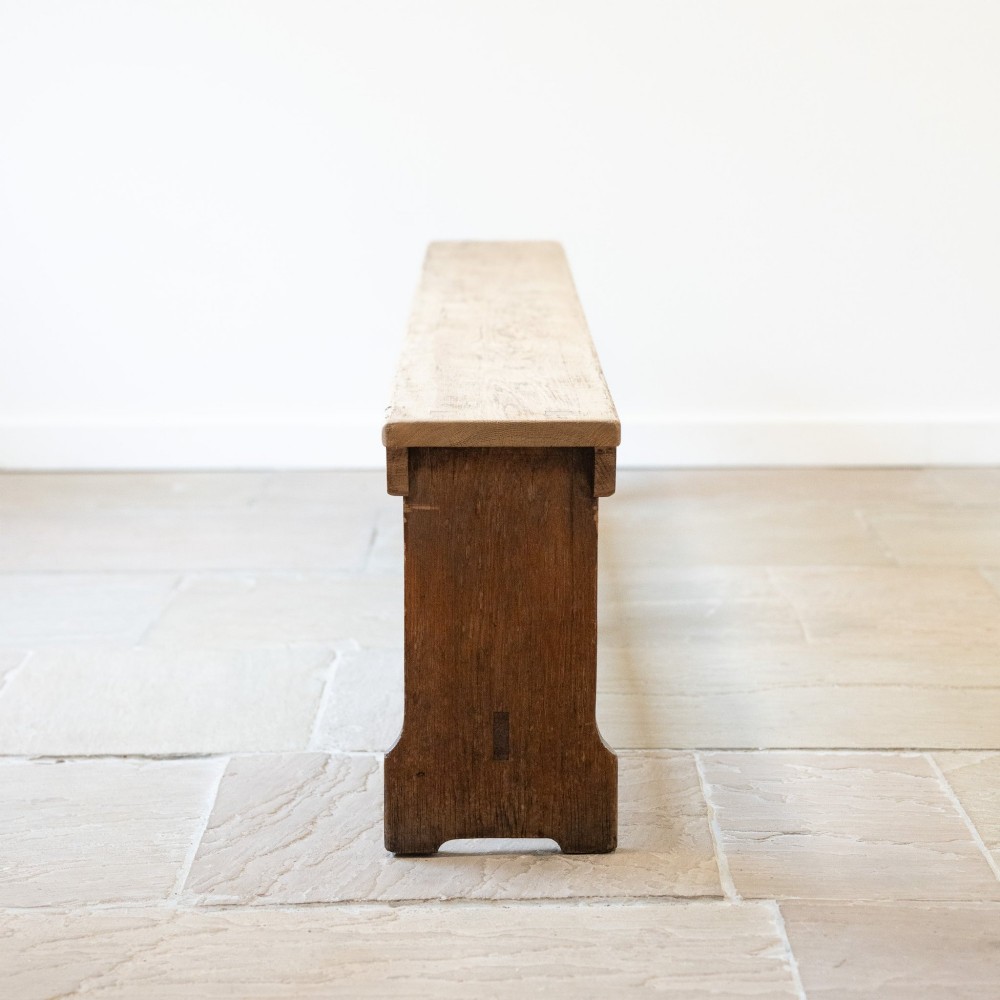 A long English oak refectory bench featuring a rectangular seat supported by three slab legs connected by a low central stretcher. View II