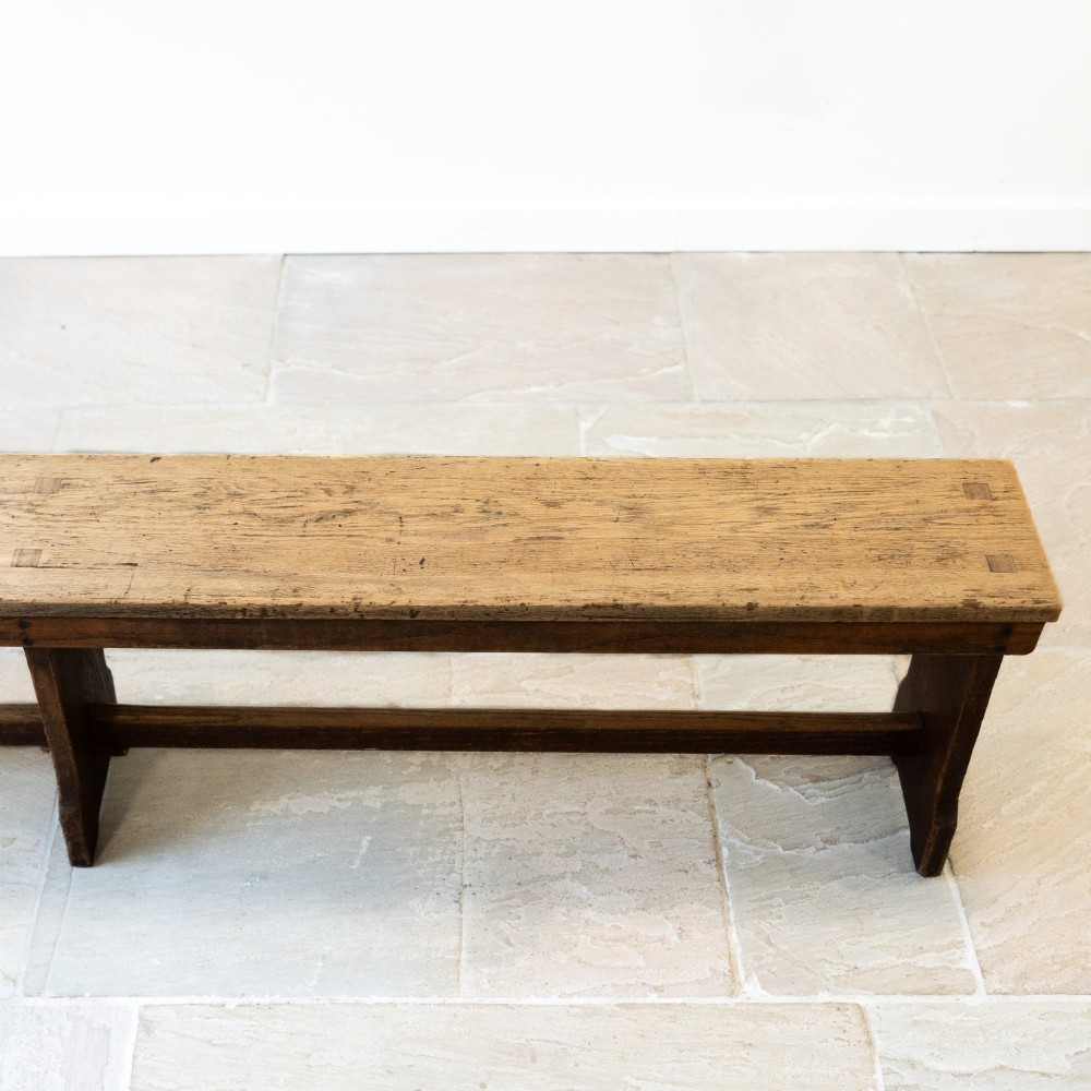 A long English oak refectory bench featuring a rectangular seat supported by three slab legs connected by a low central stretcher. View III