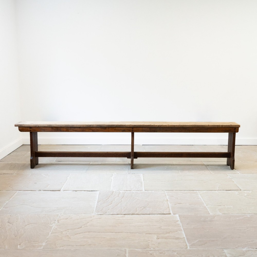 A long English oak refectory bench featuring a rectangular seat supported by three slab legs connected by a low central stretcher. View IV