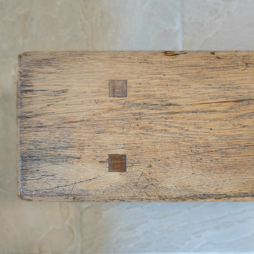 A long English oak refectory bench featuring a rectangular seat supported by three slab legs connected by a low central stretcher. View IX