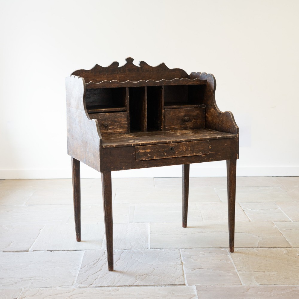 A dark brown antique French provincial clerk desk featuring a scalloped gallery back, pigeonholes, small interior drawers, and square tapered legs.