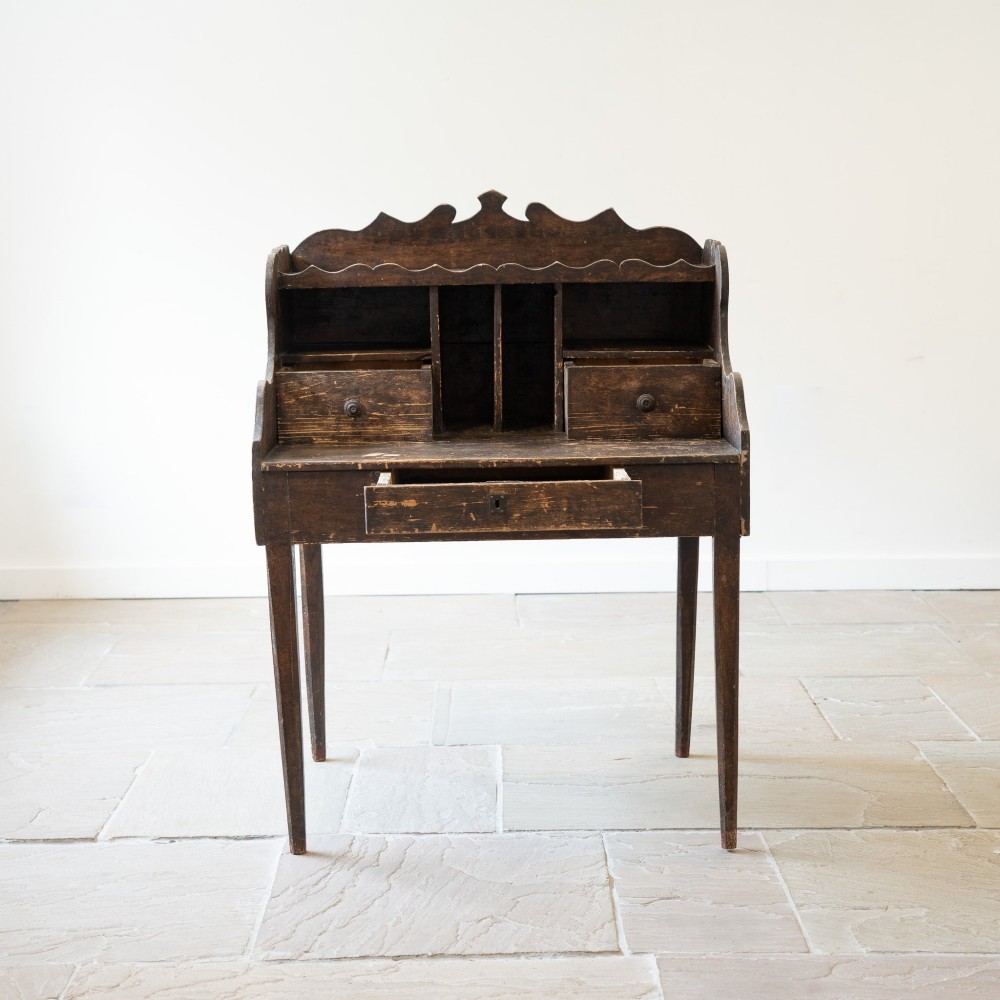 A dark brown antique French provincial clerk desk featuring a scalloped gallery back, pigeonholes, small interior drawers, and square tapered legs. View III
