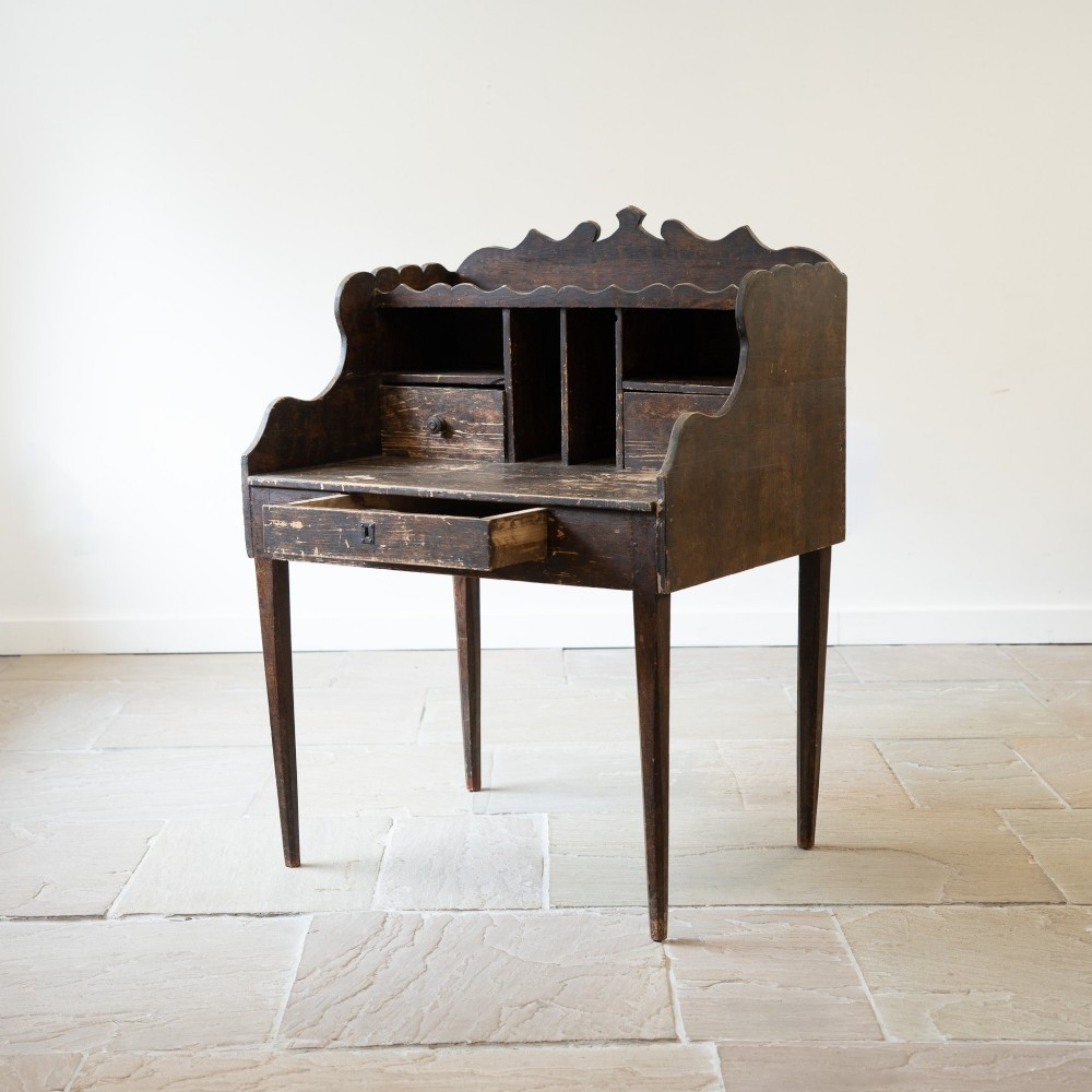 A dark brown antique French provincial clerk desk featuring a scalloped gallery back, pigeonholes, small interior drawers, and square tapered legs. View VII