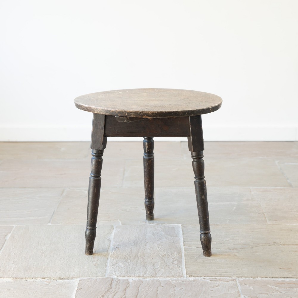 An English nineteenth-century dark brown wooden cricket table featuring a circular top and three turned legs.