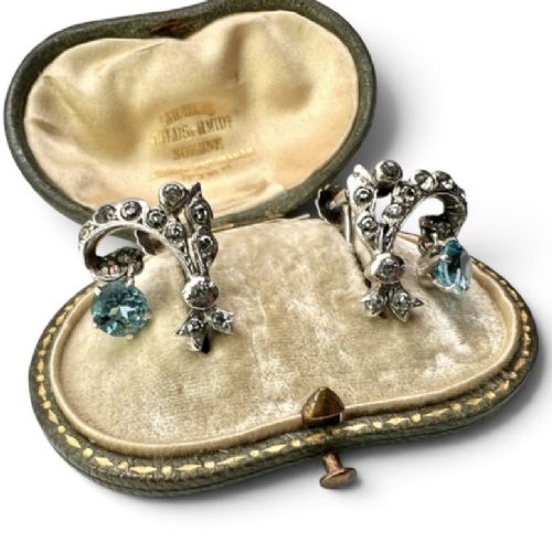 Pair of Edwardian silver screwback drop earrings featuring scrollwork set with clear paste stones and suspended light blue glass gems. View II