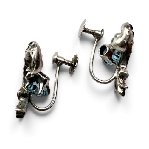 Pair of Edwardian silver screwback drop earrings featuring scrollwork set with clear paste stones and suspended light blue glass gems. View IV