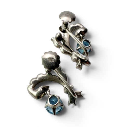 Pair of Edwardian silver screwback drop earrings featuring scrollwork set with clear paste stones and suspended light blue glass gems. View V