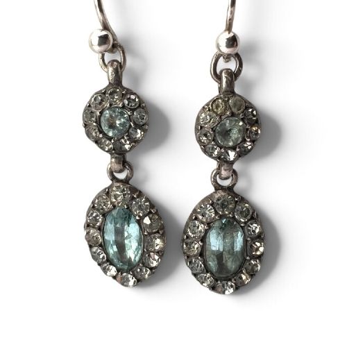 A pair of antique silver drop earrings featuring oval light blue paste central stones surrounded by clear paste halos suspended from wire hooks. View III