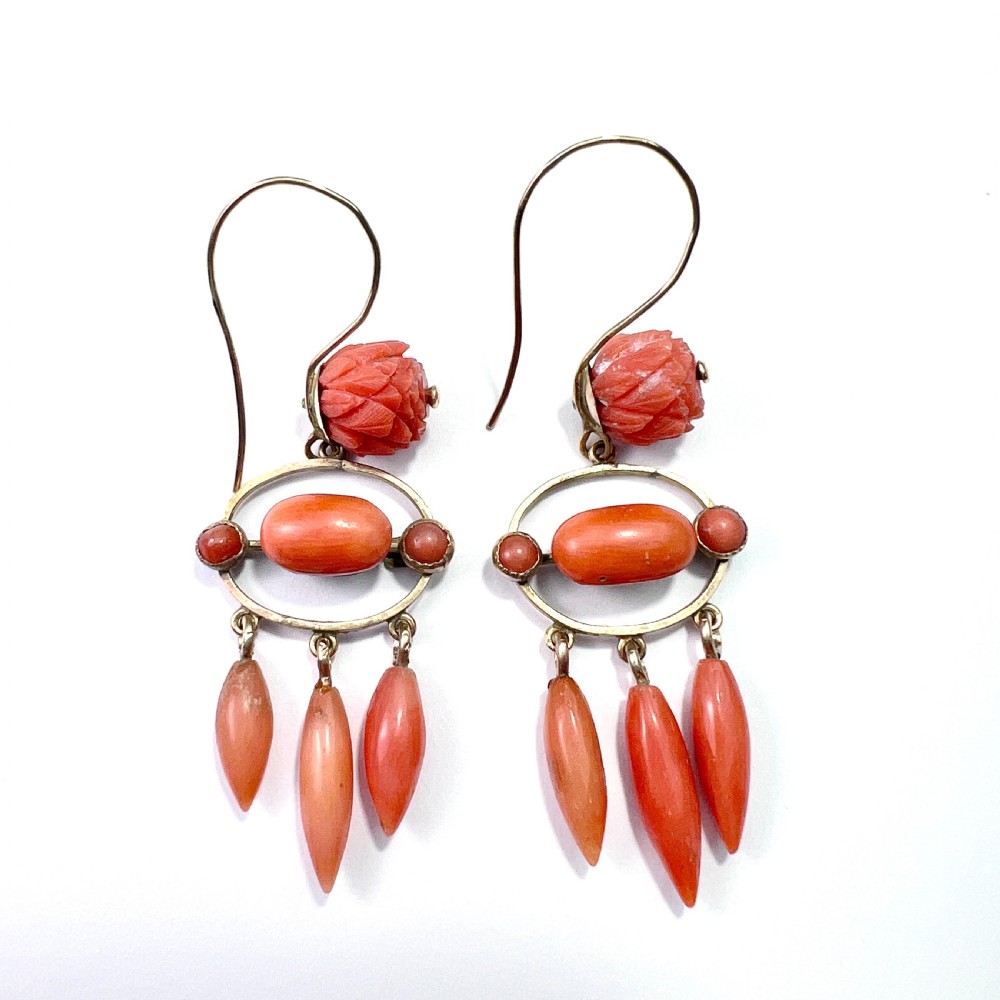 A pair of antique 9ct gold drop earrings featuring carved coral flowers, oval coral cabochons, and dangling coral torpedo drops.