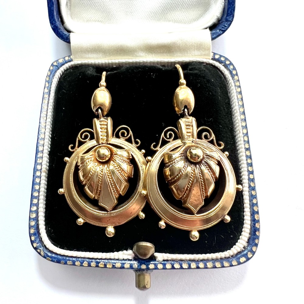A pair of Victorian 18ct yellow gold drop earrings featuring detailed acanthus leaf motifs suspended within circular outer hoops.