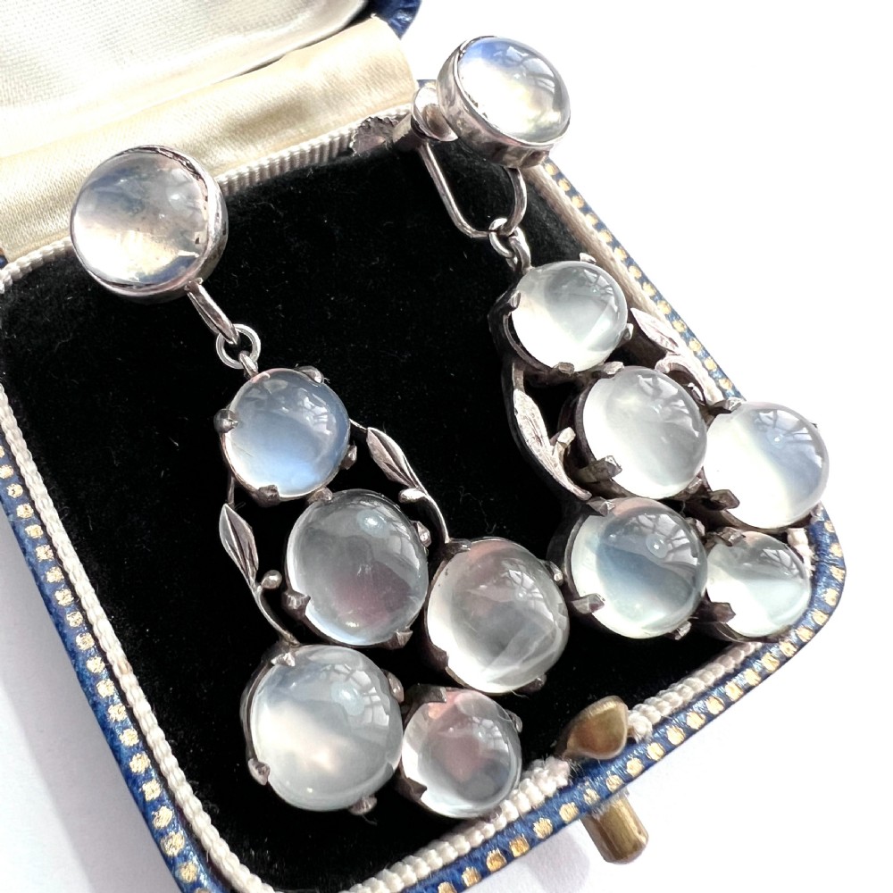A pair of silver Arts and Crafts screwback drop earrings set with translucent cabochon moonstones arranged in a cluster with leaf motifs.