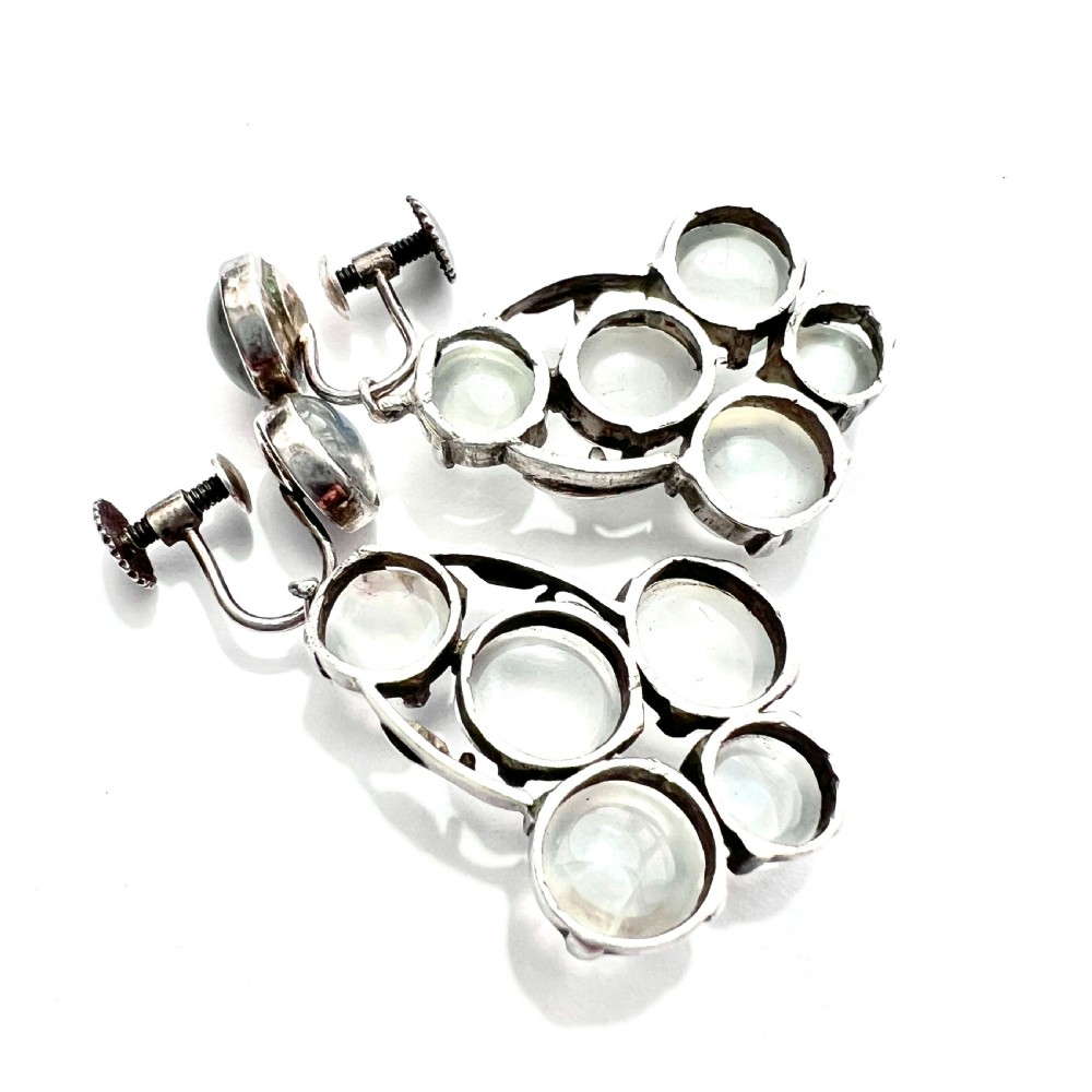 A pair of silver Arts and Crafts screwback drop earrings set with translucent cabochon moonstones arranged in a cluster with leaf motifs. View V