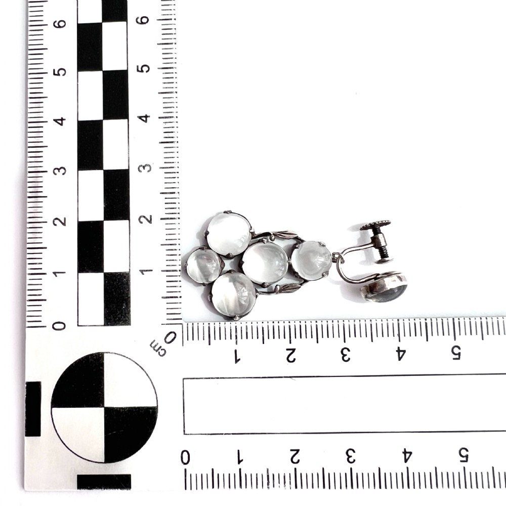 A pair of silver Arts and Crafts screwback drop earrings set with translucent cabochon moonstones arranged in a cluster with leaf motifs. View VI