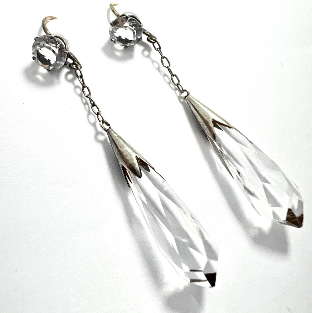 A pair of Edwardian drop earrings featuring faceted round rock crystals connected via fine chains to elongated faceted teardrop rock crystal pendants set in silver metal.