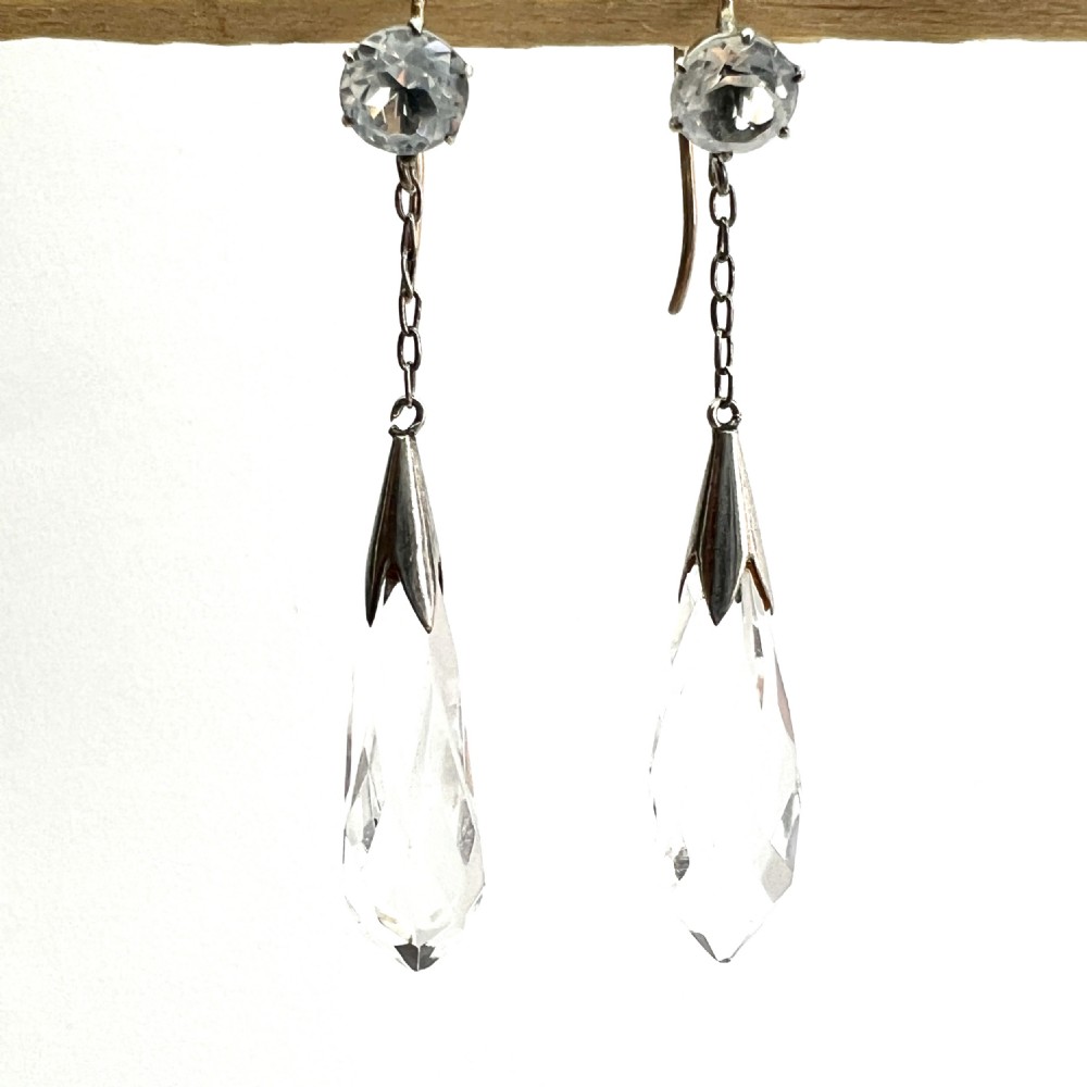 A pair of Edwardian drop earrings featuring faceted round rock crystals connected via fine chains to elongated faceted teardrop rock crystal pendants set in silver metal. View IV