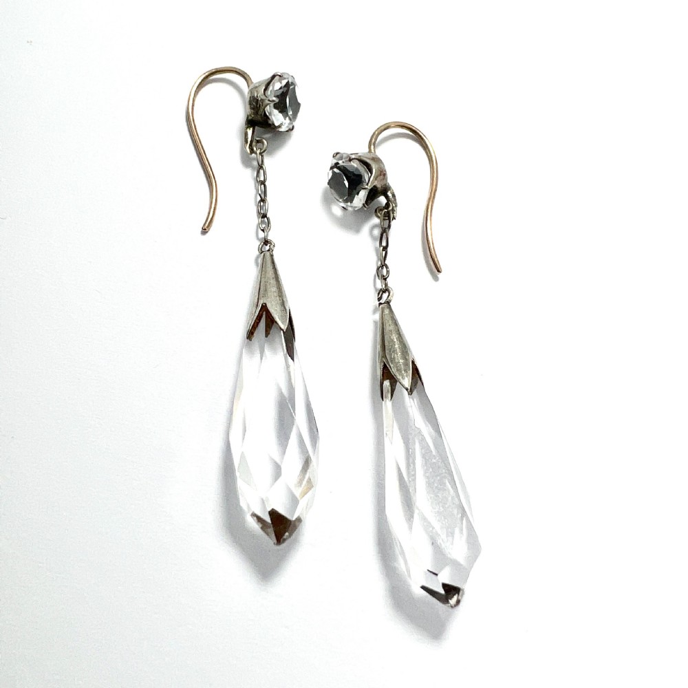 A pair of Edwardian drop earrings featuring faceted round rock crystals connected via fine chains to elongated faceted teardrop rock crystal pendants set in silver metal. View V